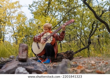 in the autumn park the boy scout sits on a log with a guitar in his hands