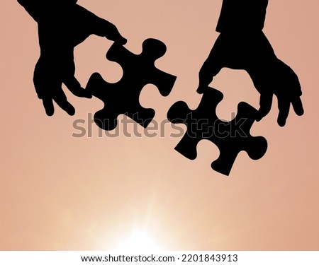 black silhouette of two Puzzles in male hand isolated on yellow or red sunny sky background.  2 jigsaw Puzzles with human hands .  sun rays. orange Sunrise. 