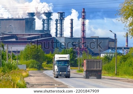 Smoking chimneys of a steel or chemical plant emitting toxic smoke against the background of trucks moving along a city street out of focus. Air pollution in the city, greenhouse effect. Royalty-Free Stock Photo #2201847909