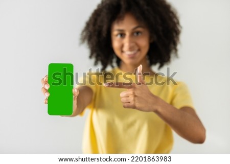 Portrait of a black woman holding a big green screen smartphone in her hand, showing and pointing at the device, banner