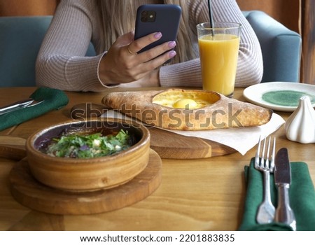 People, technology and food. A girl in a Georgian restaurant at the table is holding a smartphone in her hands. Women's hands with manicure.