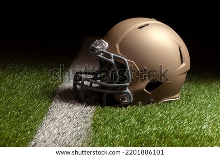 Gold football helmet on grass field with stripe and spot lighting