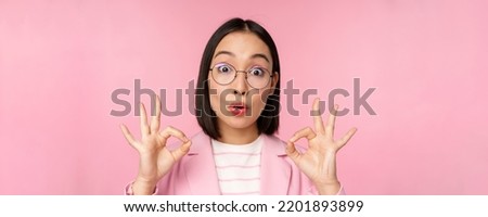 Close up portrait of business woman looks impressed and shows okay sign in approval, recommending company. Young corporate lady in glasses shows ok gesture, pink background
