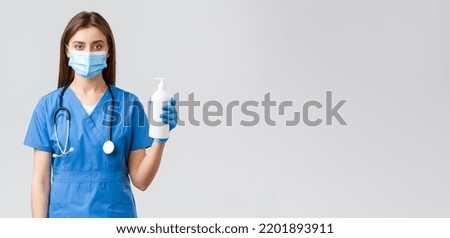 Covid-19, preventing virus, health, healthcare workers and quarantine concept. Professional female nurse in clinic, doctor wearing medical mask, scrubs, holding hand sanitizer or soap