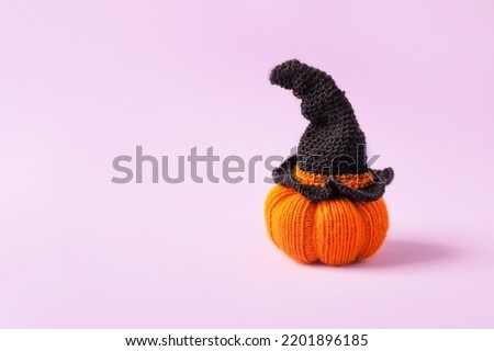 Knitted orange pumpkin with a black witch hat on an purple background, autumn composition, front view. Halloween concept.