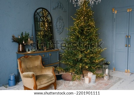 Christmas and New Year decorate the dark interior of the room. A festively decorated room with a fireplace, an armchair and a mirror. Festive Christmas night with lights on the Christmas tree gifts