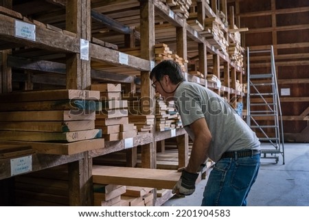 Kingston, NH, US-September 12, 2022: Man choosing lumber in local lumber yard with stacks of hardwoods and softwoods in background. Royalty-Free Stock Photo #2201904583
