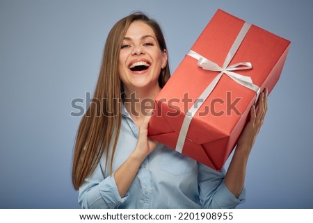 Happy woman holding big red gift box. Isolated female portrait on blue.