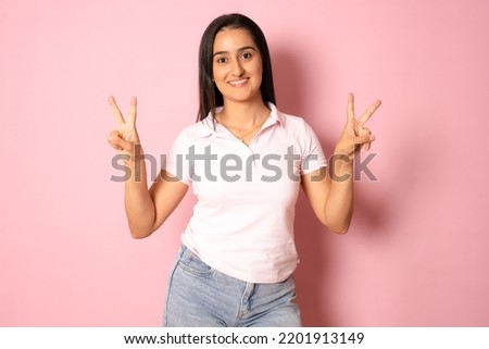 Young mixed race hispanic woman isolated showing victory sign and smiling broadly isolated over pink background.