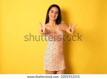 Young mixed race hispanic woman isolated showing victory sign and smiling broadly isolated over yellow background.