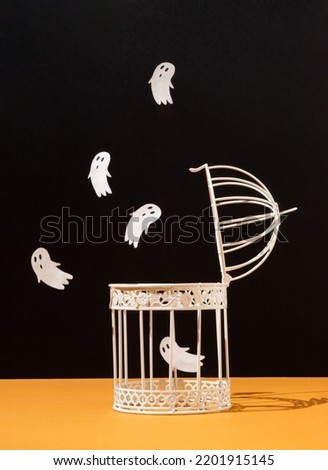Halloween concept with bird cage and ghosts on black and orange background. Scary and spooky concept. Modern aesthetic.