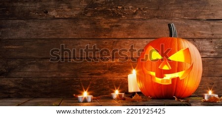 Halloween pumpkin candles and dry maple leaves on wooden background