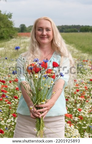 beautiful middle-aged blonde woman stands among a flowering field of poppies 