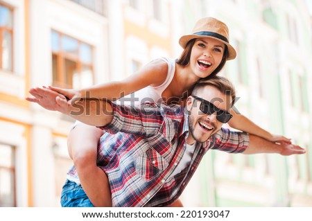 Happy loving couple. Happy young man piggybacking his girlfriend while keeping arms outstretched  Royalty-Free Stock Photo #220193047
