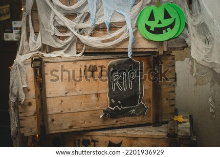 Green bright halloween pumpkin with painted nose, mouth and eyes on wooden box with gauze as web and tombstone with RIP inscription. Handmade images of scary face and grave. DIY Halloween decoration