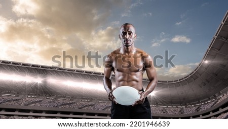 Composition of shirtless male rugby player holding rugby ball over sports stadium. sport and competition concept digitally generated image.