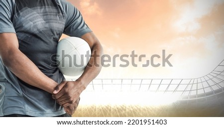 Composition of male rugby player holding rugby ball over sports stadium. sport and competition concept digitally generated image.