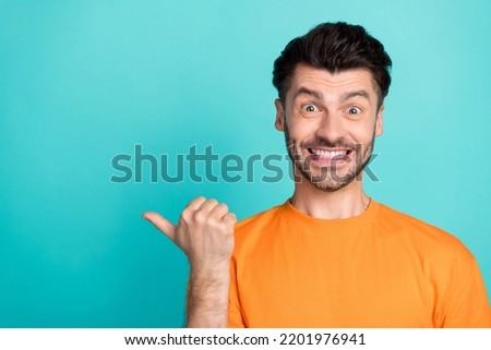 Closeup photo of young attractive handsome toothy funny face positive smile thumb pointing empty space nice offer amazed isolated on aquamarine color background