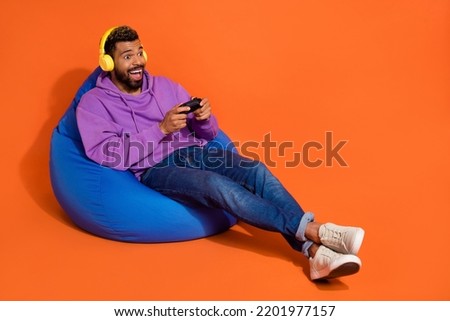 Full size photo of overjoyed man sit bag hand hold controller play games isolated on orange color background