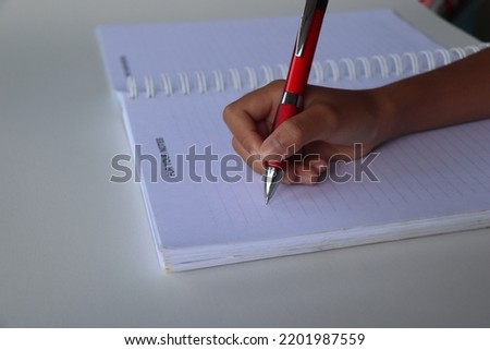 Cropped shot of an unrecognizable female hands holding and using a pen on the note book isolated on a black background