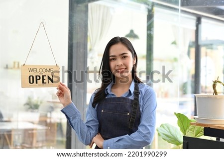 Beautiful and charming young Asian female coffee shop owner or barista standing in front of her coffee shop or restaurant entrance. Business entrepreneur concept