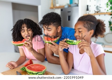 Young Family eating watermelon and having fun. Mixed race family in kitchen together eating a watermelon slice.