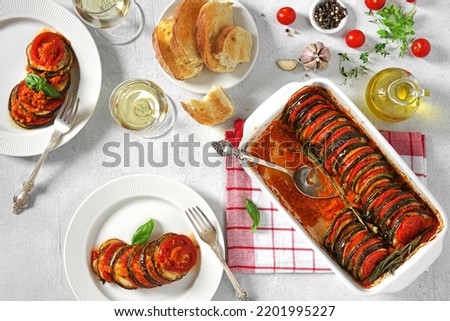 Delicious ratatouille in baking dish and plates on white table, and glasses of wine. dinner concept
