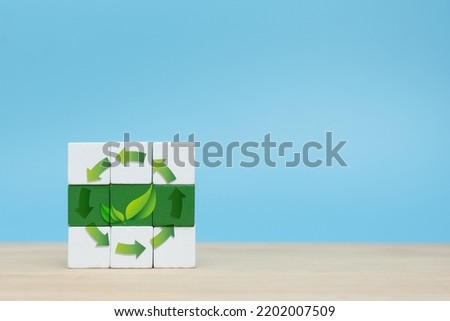 Recycle symbols with green leaves on wooden cube on table and blue background