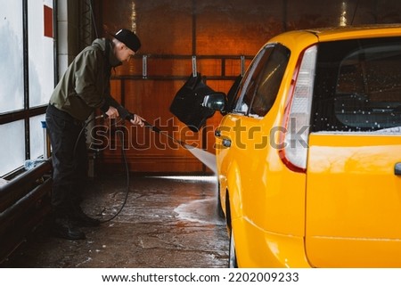 Washing a yellow car at a contactless self-service car wash. Washing a sedan car with foam and high-pressure water. Spring cleaning at the car wash. Royalty-Free Stock Photo #2202009233