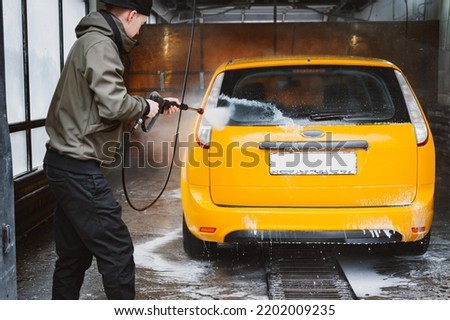 Washing a yellow car at a contactless self-service car wash. Washing a sedan car with foam and high-pressure water. Spring cleaning at the car wash. Royalty-Free Stock Photo #2202009235