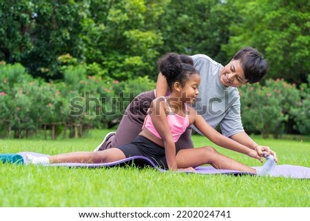 Half-African Thai doing stretching yoga with an Asian mother practicing poses on a yoga mat in the garden. Fitness concept.