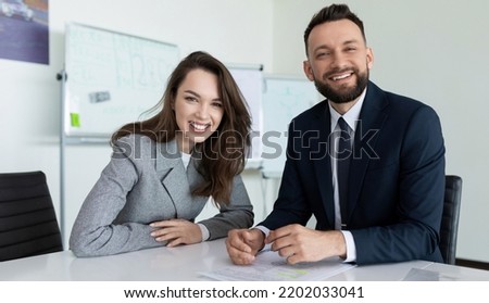 man and woman employees of the company in presentable business clothes with a smile look at the camera while sitting at the table Royalty-Free Stock Photo #2202033041