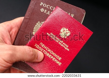 Hand holding russian pension certificate and passport. Russian translation - Pension Fund of Russian Federation. Pension Certificate.