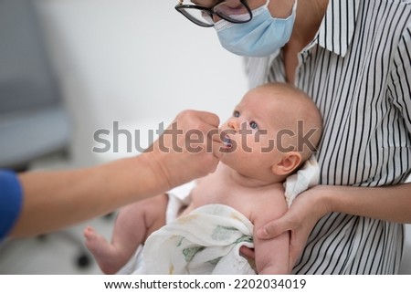 Pediatrician administring oral vaccination against rotavirus infection to little baby in presence of his mother. Children health care and disease prevention Royalty-Free Stock Photo #2202034019