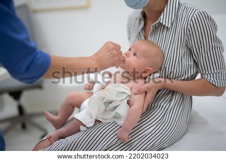 Pediatrician administring oral vaccination against rotavirus infection to little baby in presence of his mother. Children health care and disease prevention Royalty-Free Stock Photo #2202034023