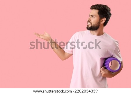 Young man with foam roller showing something on pink background