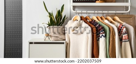 Hanger with different knitted sweaters near light wall in room