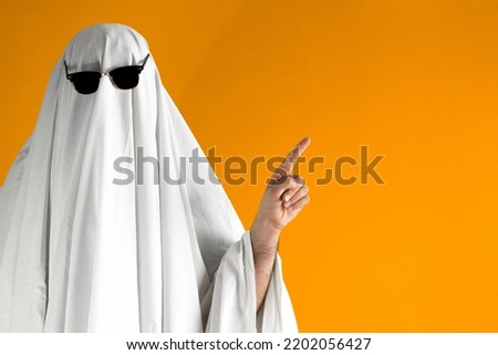 Person in Halloween costume of ghost with sunglasses points away Royalty-Free Stock Photo #2202056427