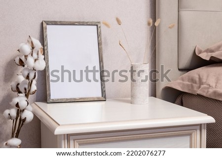 Template with photo frame on a bedside table. Bouquet of Lagurus. Cotton. Sunlight from the window.