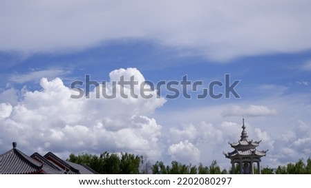 A view of the sky with many large white clouds and the bottom edge of the ground is the roof and Chinese temple construction objects with trees below the picture.