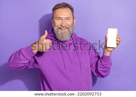 Portrait of cheerful optimistic good mood man dressed purple hoodie hold smartphone approve like isolated on violet color background