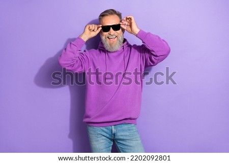 Portrait of handsome retired positive man with white gray beard wear purple hoodie hold sunglass isolated on violet color background