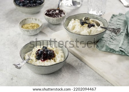 Two grey bowls with plain white icelandic diary breakfast skyr with jam, fresh blueberries, hemp seeds on marble board on grey background