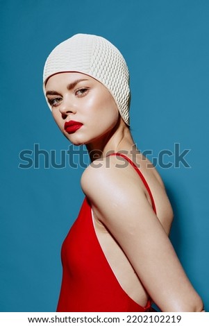 Charming Woman in a bathing cap in a red swimsuit, turning around from behind her shoulder, posing on a blue sea background. Close-up portrait Royalty-Free Stock Photo #2202102219