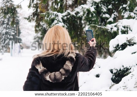 Winter landscape, Christmas trees in the snow. woman with mobile phone is photographed and shows the surrounding nature.