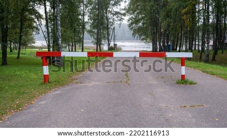 Entry is prohibited. Red and white barrier on the road. The road leads to the lake.