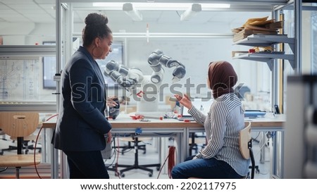 Black Chief Engineer Helps Arabic Young Scientist with Work on Laptop Computer In Office. Professionals Write Program for Robot Arm. People Designing Automated Robotic Systems.