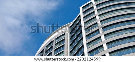 Office skyscraper high business building on blue sky background, looking up tall glass windows and steel high rise modern building. Multistory glass building with cloudy blue sky background Royalty-Free Stock Photo #2202124599