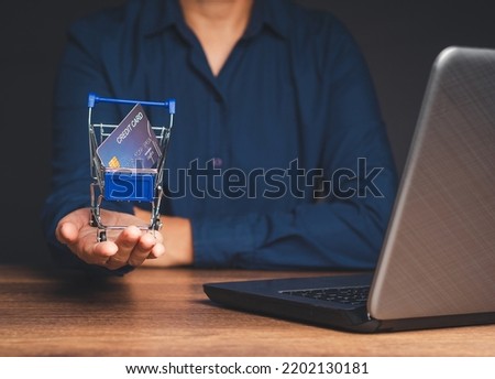 Man in a blue shirt holding a mini shopping trolley with a credit card mockup while sitting at the table in the office. Concept of online shopping. Close-up photo