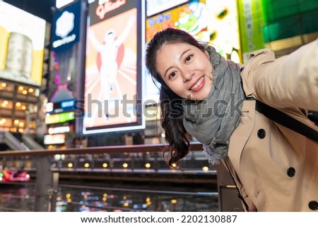 cheerful Asian Japanese girl taking self portrait picture with the illuminated glico man at background near doutonbori river and Shinsaibashisuji shopping street in Osaka japan at night Royalty-Free Stock Photo #2202130887